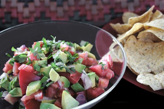 a bowl of chunky salsa with freshly chopped tomatoes, red onion, avocados, and cilantro with tortilla chips alongside