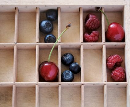 fresh cherries, blueberries and raspberries in the compartments of a wood type case