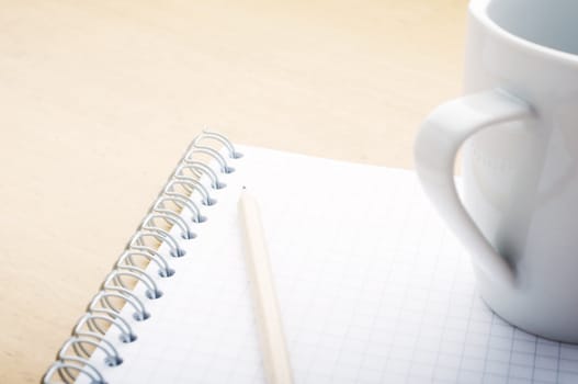 Pencil on the green spiral notebook with coffee cup