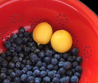 fresh blueberries and lemons in a bright red colander
