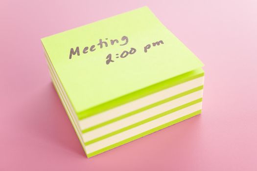 Pile of sticky notes with meeting reminder text over a pink table