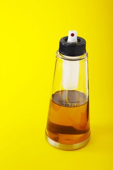 Spray bottle of olive oil on the yellow background