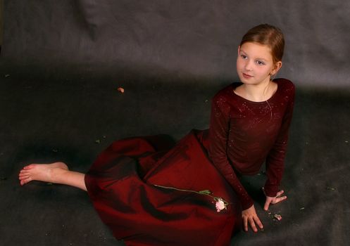 The girl in a red dress and barefoot sits on a floor in studio