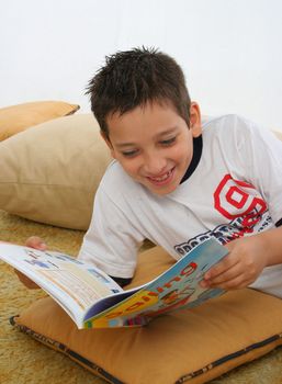 Boy in a room reading a book over a carpet. He is smiling and looks amused. Visit my gallery for more images of children

