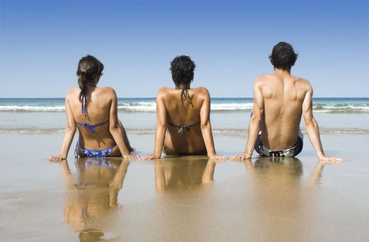 Three best friends seated on the sand having fun on the beach