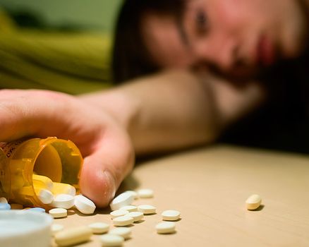 A young man slumped over with a bottle of various prescription pills in his hand.