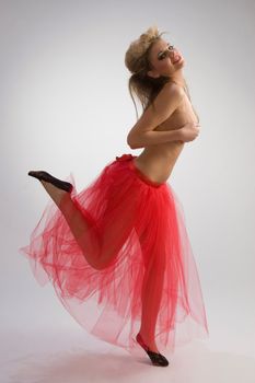 Beautiful woman in red diaphanous skirt dancing on grey background