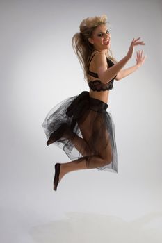 Beautiful woman in black diaphanous skirt jumping on grey background