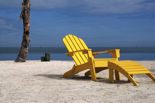 A wooden yellow recliner sits on a beautiful tropical beach