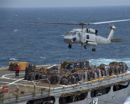 An SH-60 lifts a cargo pallete from a supply ship