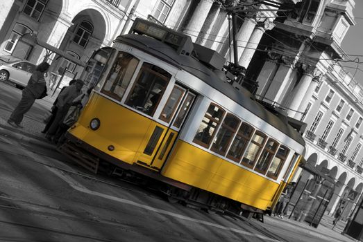 A yellow street car sits at a stop, waiting to pick up passengers on a busy city street