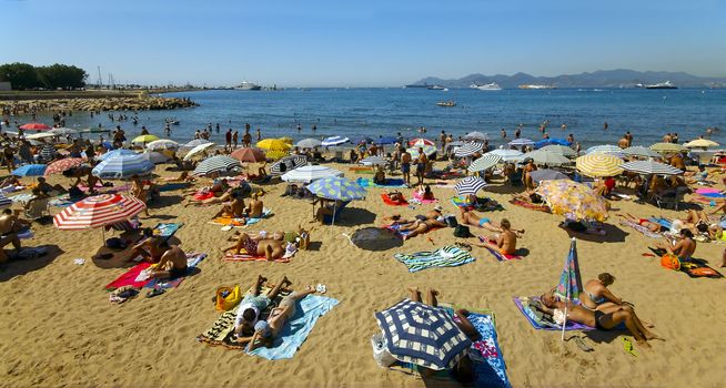 A crowd of vacationers enjoy the warm beaches of Cannes, France during the summer