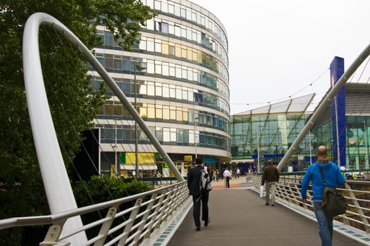 Office workers going to work towards glass building and crossing a modern white bridge