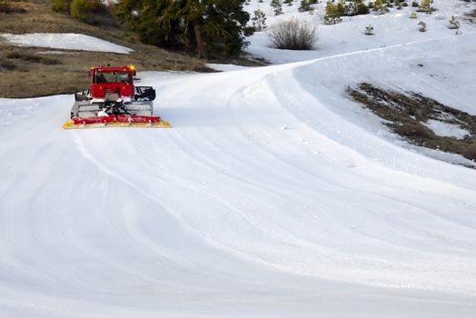 A red snow plow drives up a wintry mountain