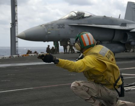 A Naval Officer signals for an F-18 Hornet to launch on board an aircraft carrier
