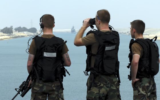 A group of soldiers stand guard on a warship as it passes through the Suez Canal