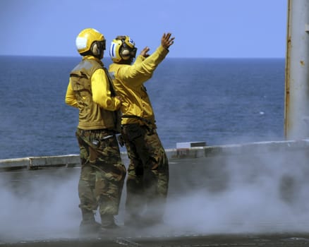 Two sailors intently taxi a waiting aircraft on to a waiting catapult onboard an aircraft carrier