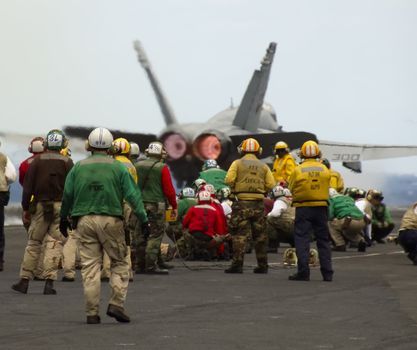 A large group of sailors watch an F-18 Hornet launch from an aircraft carrier