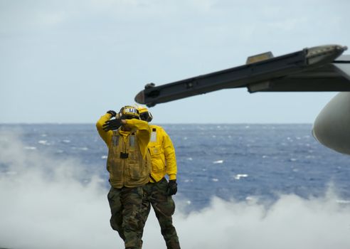 Two sailors direct an F-18 Hornet on the flight deck of an aircraft carrier