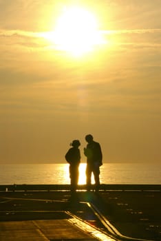 Two sailors converse at the end of a long day on an aircraft carrier