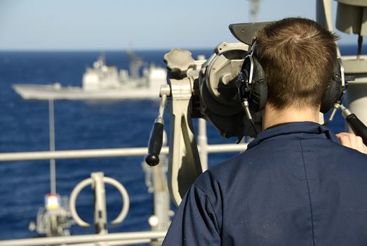 A Sailor stands his watch post and observes a passing warship