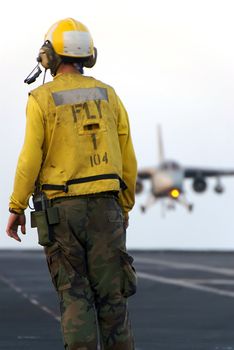 A sailor watches as a naval aircraft lands aboard an aircraft carrier