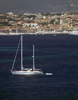 A gleaming white sailboat sits off a beautiful coastline