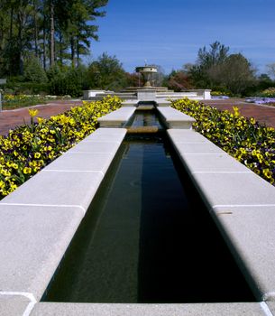 A cool and refreshing pool lined by beautiful flowers sits infront of a fountain