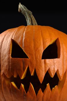 Closeup image of a carved evil pumpkin against a black background.
