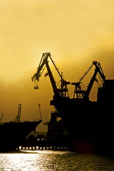 Two cranes sit at rest at an industrial shipyard
