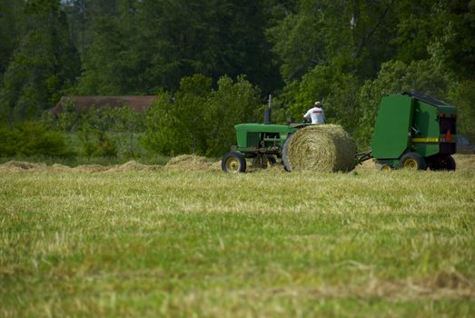 A farmer plows his fields using a green tractor