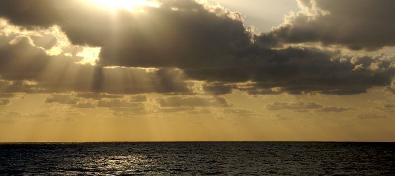 The golden rays of a sunset at sea bursts through the clouds