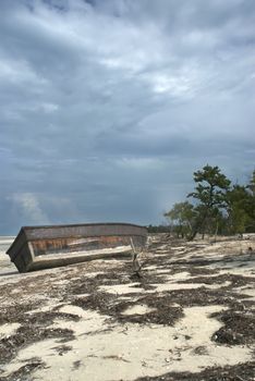 An abandoned boat sits on a tropical beach as a storm approaches