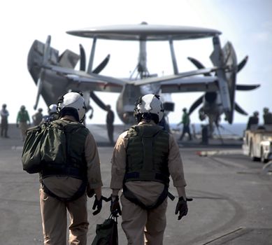 Two Pilots walk to man up their E-2 Hawkeye onboard an aircraft carrier