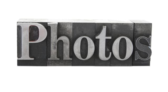 old, ink-stained metal letterpress type spells out the word 'Photos' isolated on white