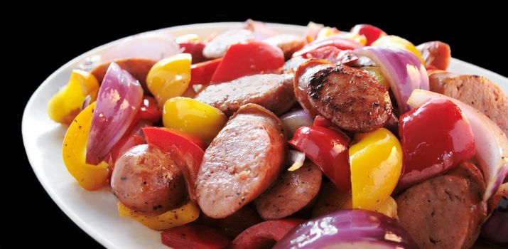Polish sausage sauteed with red and yellow bell peppers and red onion on a white platter