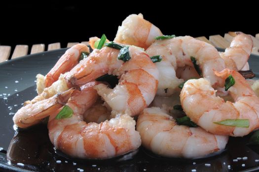 shrimp with scallions and kosher salt on a black plate on a wooden mat
