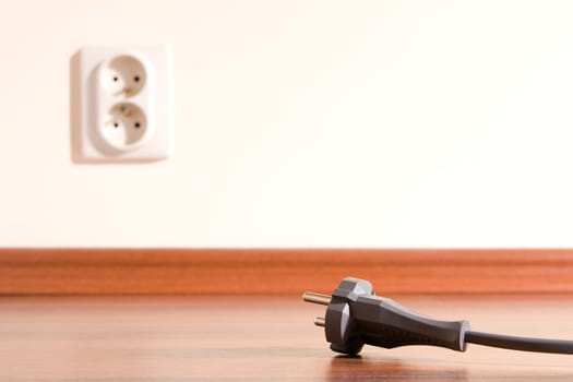 Two pin plug on the floor and electrical outlet in background