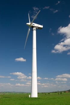 One wind turbine against blue sky with white clouds