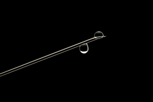 Sharp needle of a syringe with two drops of water, close-up, outline clear lines on a black background