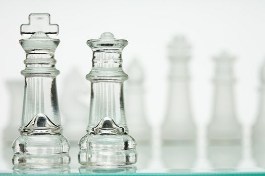 Transparent chess game on a white background. Line players in the background, blurred, over the shoulder of Kings and Queens sharp