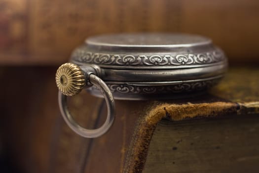 Silver pocket watch lying on a pile of old books with leather binding, macro.