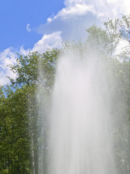 fountain against the blue sky with clouds and green trees