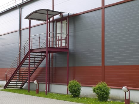 Modern building wall with stairs near green bushes in grass 