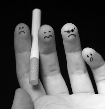 Black and white photo of fingers holding cigarette. Sad smiley painted on fingertips. Conception of addiction and anti-smoking.