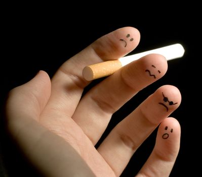 
Fingers holding cigarette. Sad smiley painted on fingertips. Conception of addiction and anti-smoking. 