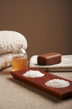 Spa salt, soap and shampoo with towels over a brown background