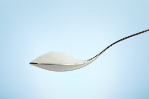 Spoon filled with fine grain sugar over blue background