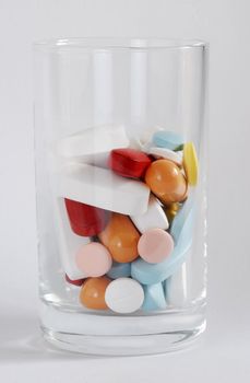 Different medicine tablets and capsules in a small glass