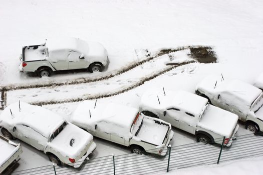 Parked cars under snow at parling lot with tracks of one gone car aerial view